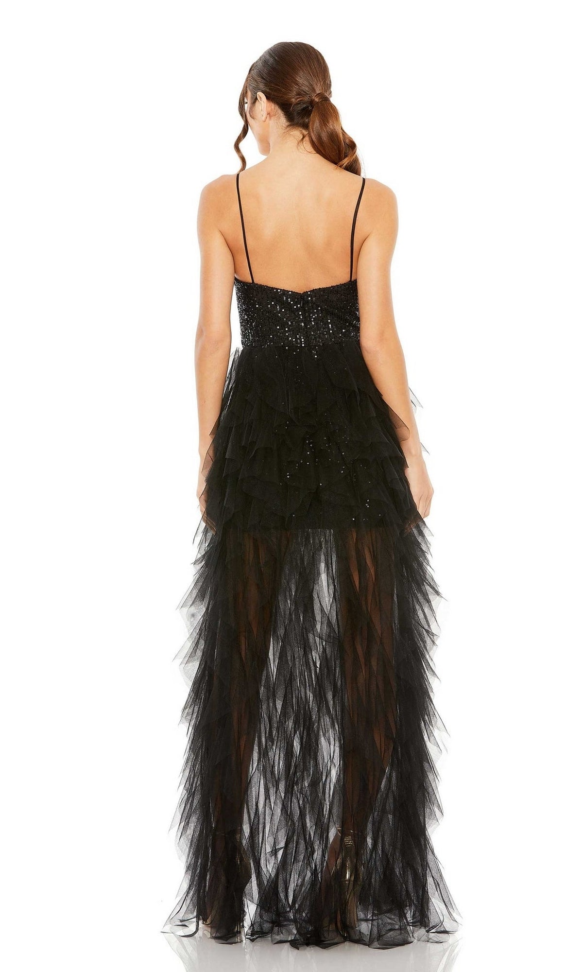 A woman with brown hair in a ponytail models the Mac Duggal 27119 Overskirt Mini Sequin Prom Dress, showing off its ruffles, thin straps, and sheer skirt from the back against a white background.